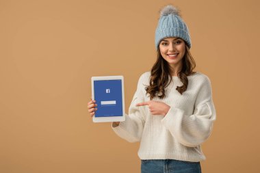Güzel esmer kız örgü şapkalı dijital tablet ile facebook app üzerinde bej izole ekranda parmak ile işaret