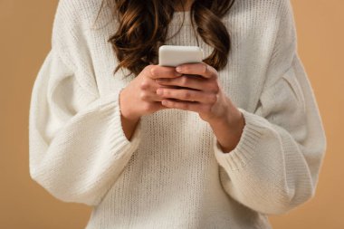 Esmer kadının beyaz kazaklı üzerinde bej izole smartphone kullanarak kırpılmış görünümü