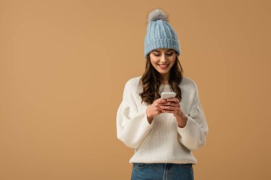 Beyaz kazaklı üzerinde bej izole smartphone kullanarak neşeli esmer kadın