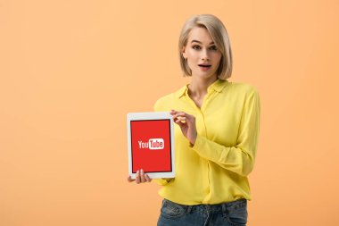 Sarı tişört üzerinde turuncu izole ekranda dijital tablet youtube uygulaması ile tutarak sürpriz genç kadın