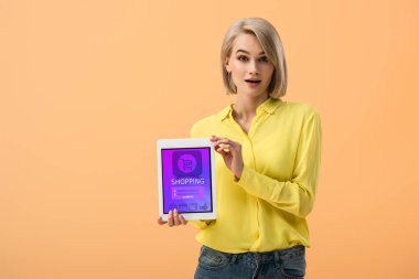 Online alışveriş uygulaması ile dijital tablet üzerinde turuncu izole ekran üzerinde tutan sürpriz sarışın kadın