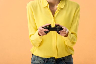 Cropped view of woman in yellow shirt holding gamepad isolated on orange clipart