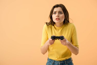 Gamepad üzerinde turuncu izole tutan korkmuş esmer genç kadın