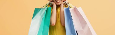 Panoramic shot of laughing girl holding shopping bags isolated on orange