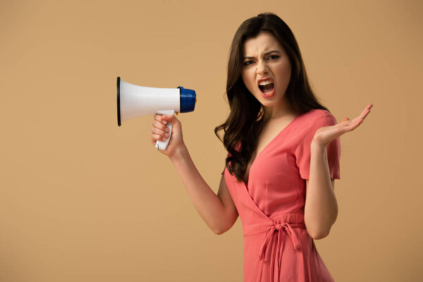 Angry brunette woman in dress holding megaphone and screaming isolated on beige