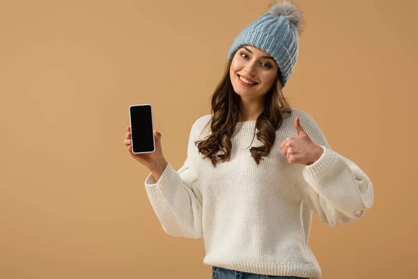 愉快的女孩在白色毛衣拿着智能手机与空白屏幕和显示拇指查出在米色 — 图库照片