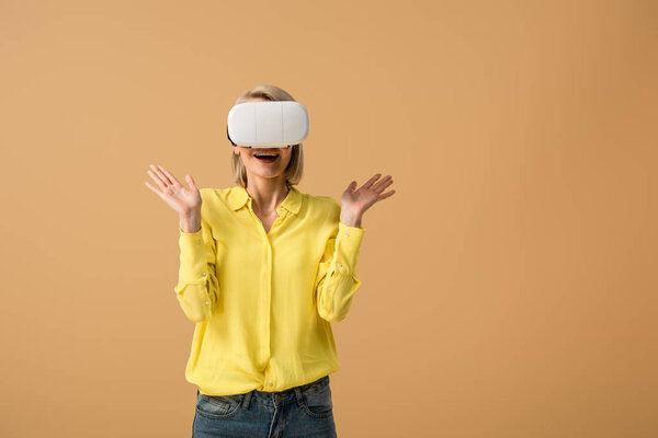 Excited blonde girl in yellow shirt and vr headset isolated on beige