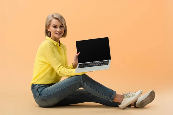 Usměvavá Blondýnka Džínách Zobrazeno Laptop Černou Obrazovkou Při Posezení Oranžové — Stock fotografie