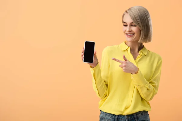 微笑的妇女在黄色衬衫指向手指在智能手机与空白屏幕查出在橙色 — 图库照片