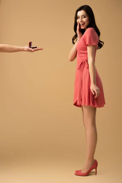 ベージュ色の背景にドレスでびっくりのブルネットの少女にプロポーズをする男のトリミング ビュー — ストック写真