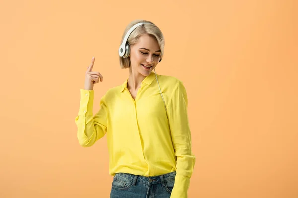 快乐的金发碧眼的女人在黄色衬衫听音乐耳机隔离橙色 — 图库照片
