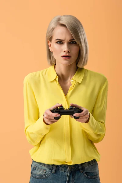 担心的金发碧眼的女人在黄色衬衫拿着游戏板隔离橙色 — 图库照片