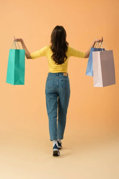 穿牛仔裤的黑发女子的背部 在橙色背景上拿着购物袋 — 图库照片