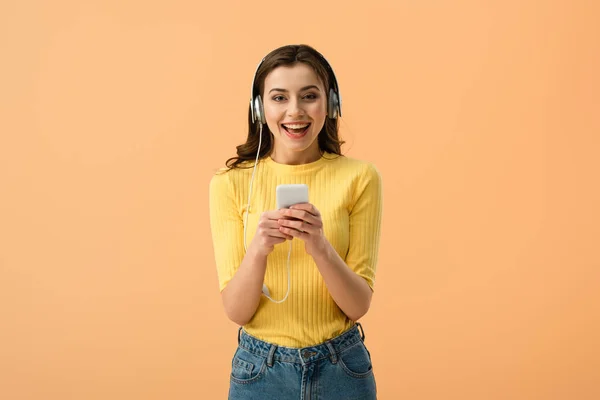 Kulaklık Üzerinde Turuncu Izole Smartphone Kullanarak Gülen Esmer Kız — Stok fotoğraf