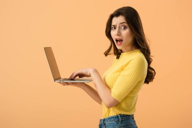 Shocked brunette young woman using laptop isolated on orange clipart