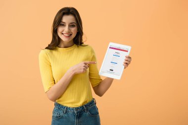 Güzel kız ile instagram app üzerinde turuncu izole ekranda dijital tablet parmak ile işaret gülüyor
