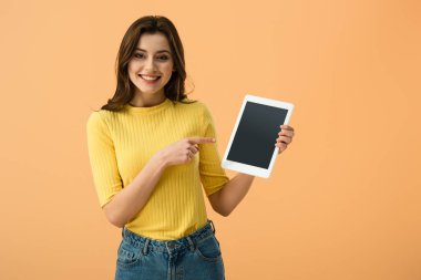 Boş ekran üzerinde turuncu izole ile dijital tablet parmak ile işaret gülümseyen esmer kız