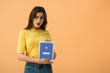 Turuncu üzerinde izole ekranda dijital tablet facebook app ile tutan sürpriz esmer genç kadın