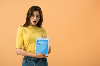 Esmer kız üzerinde turuncu izole ekranda dijital tablet twitter uygulaması ile tutarak şaşırttı