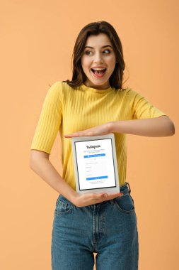 Esmer kız üzerinde turuncu izole ekranda dijital tablet instagram app ile tutarak heyecanlı