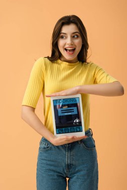 Esmer kız üzerinde turuncu izole ekranda dijital tablet rezervasyon uygulaması ile tutarak heyecanlı