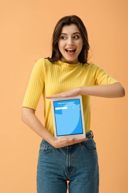 Turuncu üzerinde izole ekranda dijital tablet twitter uygulaması ile tutan genç kadın heyecanlı