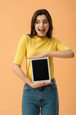 Boş ekran üzerinde turuncu izole ile dijital tablet tutan heyecanlı genç kadın
