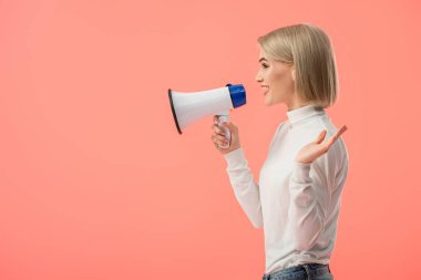 cheerful blonde woman speaking in megaphone isolated on pink 