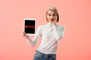pink izole ekranda netflix uygulaması ile dijital tablet tutan sürpriz sarışın kadın 