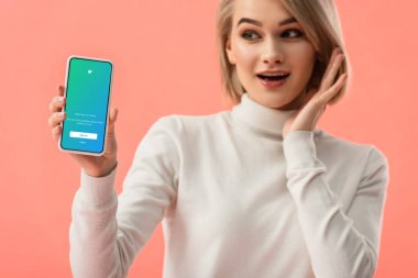 seçici odak üstünde pembe üzerinde izole perde smartphone twitter uygulaması ile tutan sürpriz sarışın kadın 