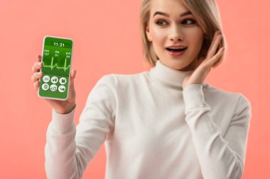 seçici odak üstünde pembe üzerinde izole perde smartphone ile sağlık app tutan sürpriz sarışın kadın 