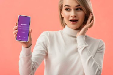 seçici odak üstünde pembe üzerinde izole perde smartphone instagram app ile tutan sürpriz sarışın kadın 