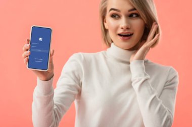 seçici odak üstünde pembe üzerinde izole perde smartphone ile facebook app tutan sürpriz sarışın kadın 