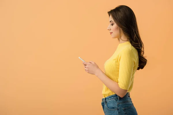 Zijaanzicht Van Mooie Brunette Meisje Met Smartphone Geïsoleerd Oranje — Stockfoto