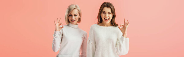 panoramic shot of attractive brunette and blonde girls showing ok sign isolated on pink 