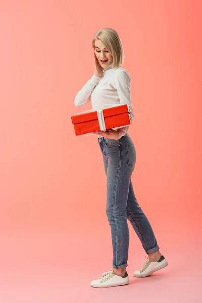 Schockierte Blonde Frau Schaut Auf Geschenkbox Auf Rosa Hintergrund — Stockfoto