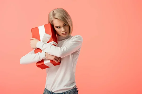 悲伤的金发女孩拥抱红色礼品盒隔离粉红色 — 图库照片