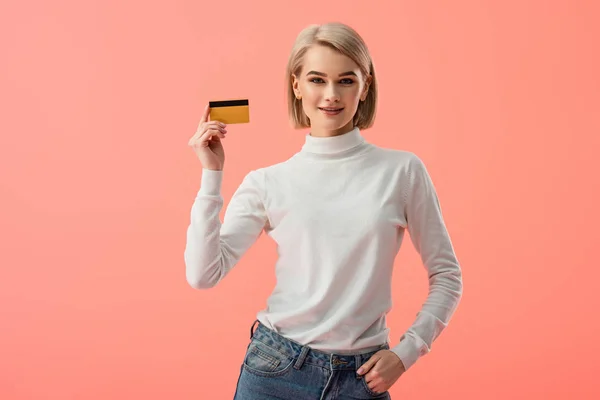クレジット カードを保持していると ピンクの隔離されたポケットで手に立って幸せな金髪の若い女性 — ストック写真