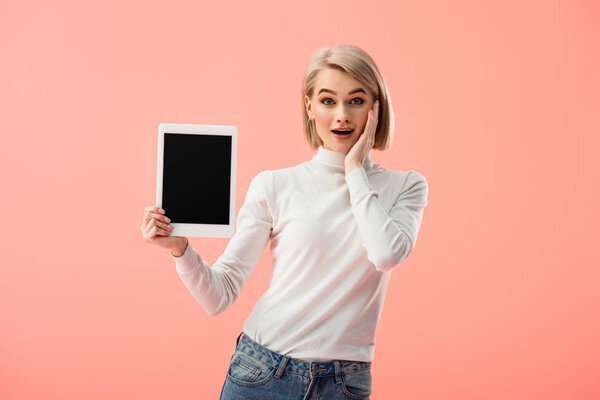 shocked blonde woman holding digital tablet with blank screen isolated on pink 