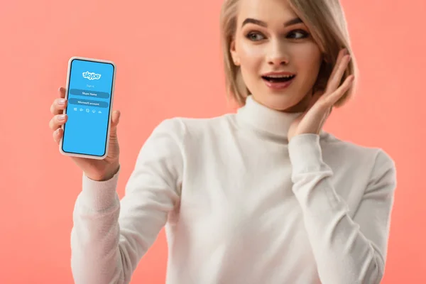 有选择的焦点惊讶的金发女子拿着智能手机与 Skype 应用程序在屏幕上隔离粉红色 — 图库照片