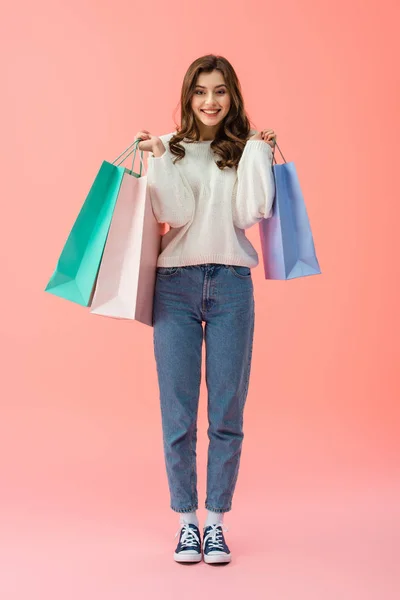 全长的笑容和有吸引力的女人拿着购物袋在粉红色的背景 — 图库照片