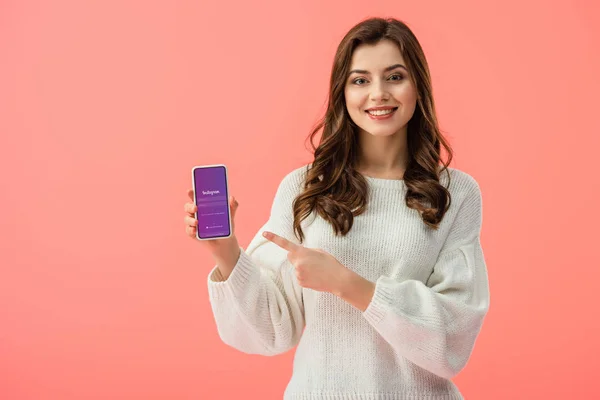 妇女在白色毛衣指向手指在智能手机与 Instagram 应用程序在屏幕上隔离在粉红色 — 图库照片