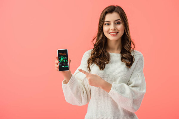 женщина в белом свитере указывая пальцем на смартфон с графиками на экране изолированы на розовый
 