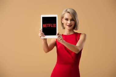 netflix uygulaması ile dijital tablet üzerinde bej izole ekran üzerinde tutan Kırmızı elbiseli güzel kadın
