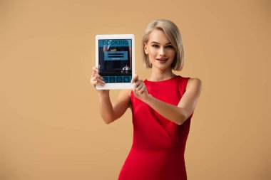 rezervasyon uygulaması ile dijital tablet üzerinde bej izole ekran üzerinde tutan Kırmızı elbiseli güzel kadın