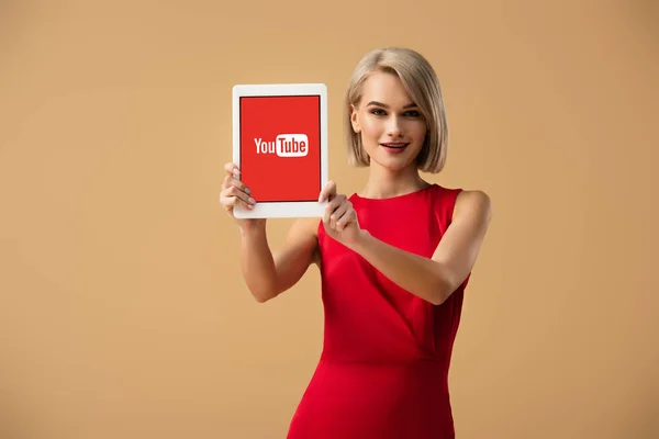 美丽的女人在红色礼服举行数字平板电脑与 Youtube 应用程序在屏幕上隔离在米色 — 图库照片