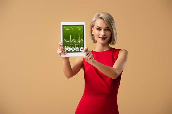 beautiful woman in red dress holding digital tablet with health app on screen isolated on beige