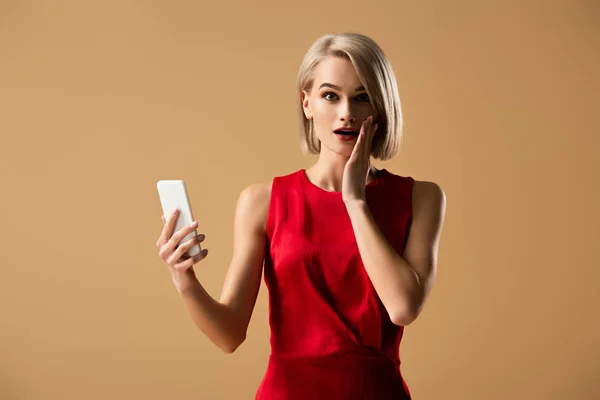 Surprised Young Woman Red Dress Holding Smartphone Isolated Beige — Stock Photo, Image