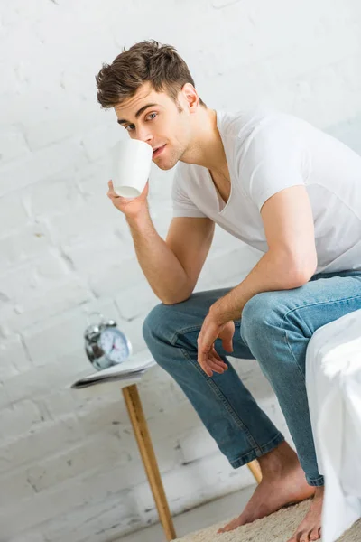 티셔츠에 청바지 침대에 앉아와 침실에서 커피를 마시는 — 스톡 사진
