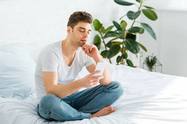 Homem Bonito Shirt Branca Jeans Sentado Cama Com Smartphone Casa — Fotografia de Stock